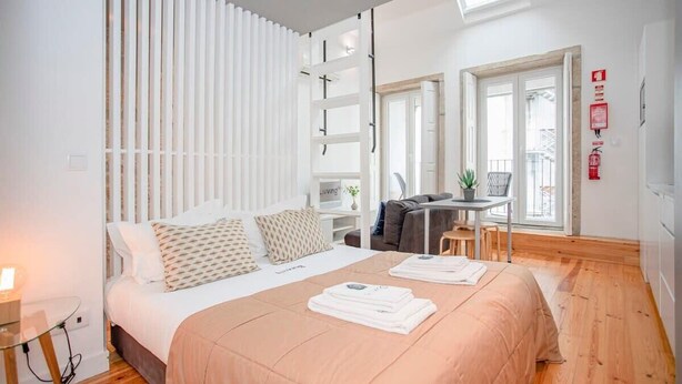 A modern bedroom with a large bed, a desk, and a balcony with a view.