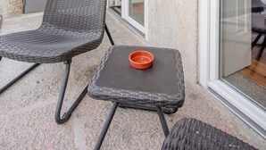 A balcony with a wicker chair and a small table, a sliding glass door, and a grey door.