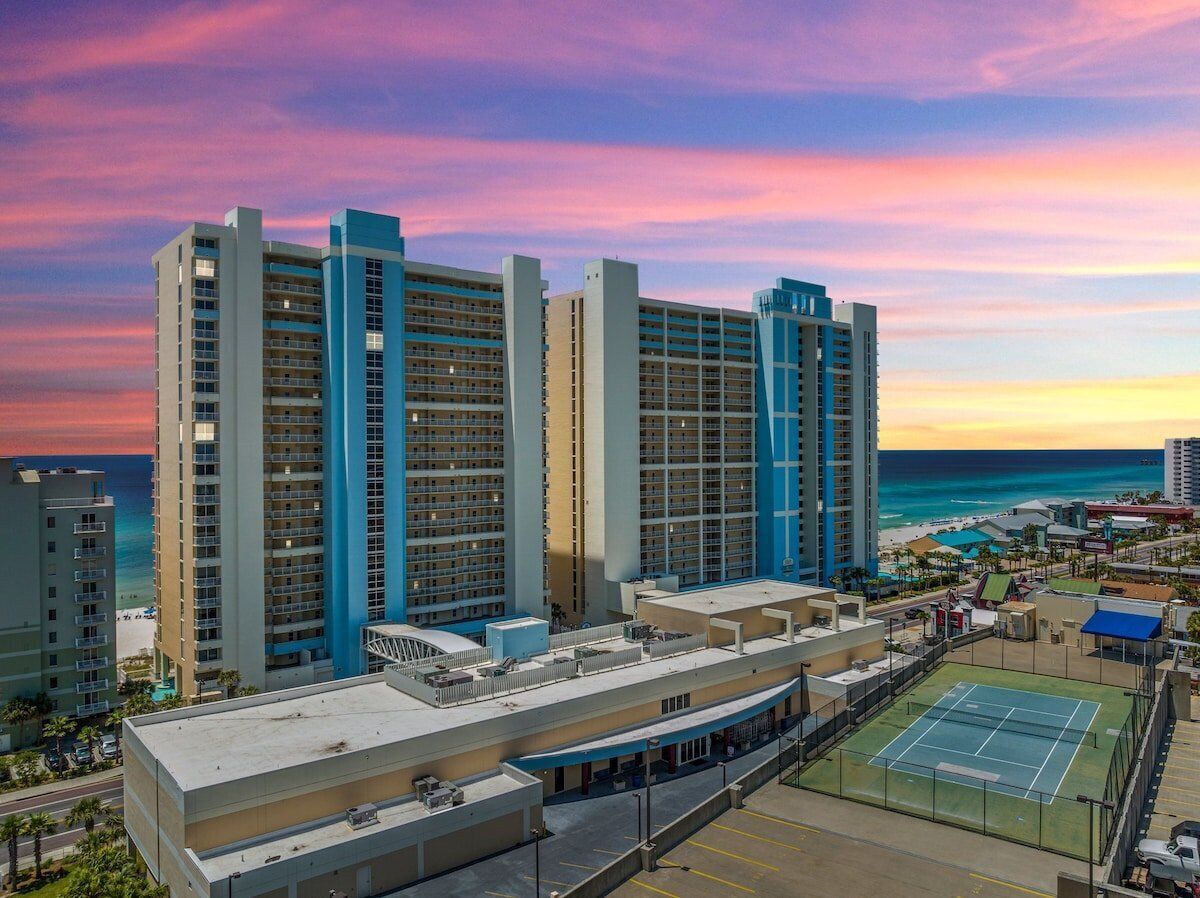 Un hotel de gran altura con varios pisos, una piscina en la azotea y una cancha de tenis.