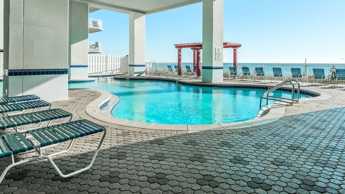 Una piscina con tumbonas y un quiosco rojo, rodeada por una terraza empedrada.