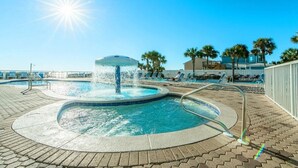 A pool area with a central water feature and surrounding lounge chairs. - Cast a Waves 512–Gulf Views–Sleeps 2 (Panama City Beach)