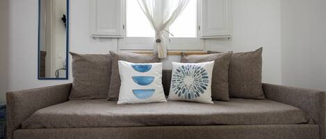 A sofa with two decorative pillows, a mirror, and a window with white shutters.