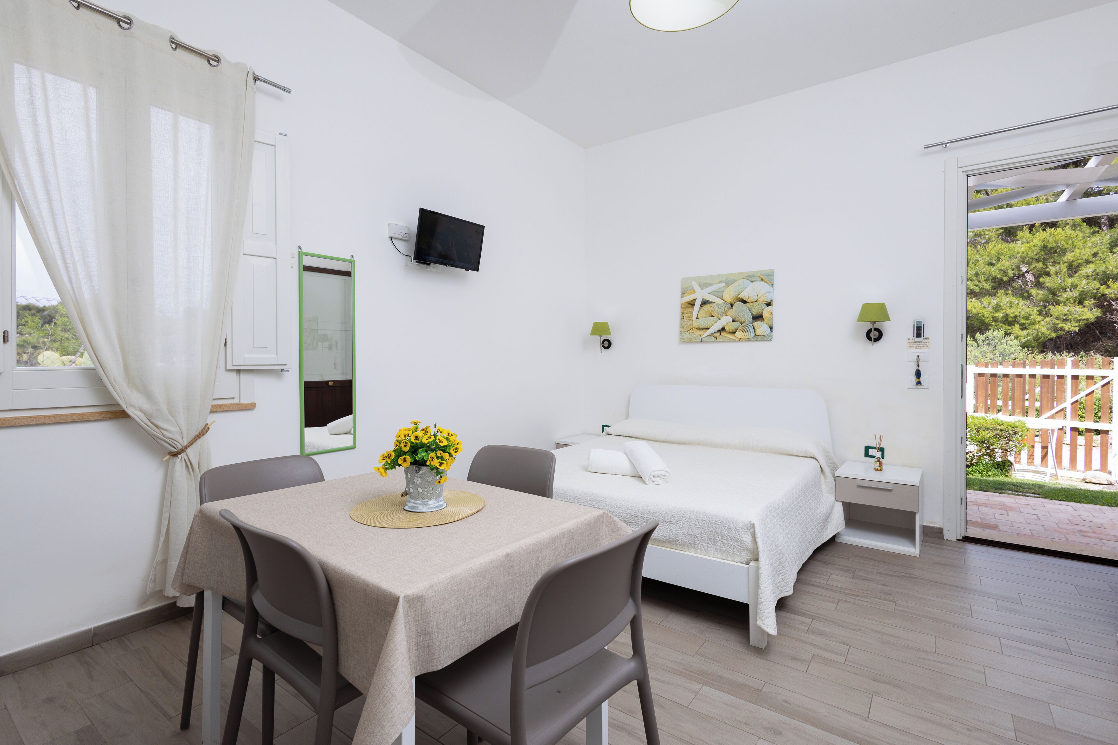 Un dormitorio con una cama, televisor, mesa con sillas y ventana con cortinas.