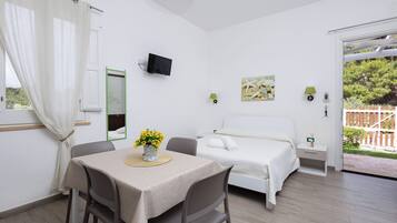 Un dormitorio con una cama, televisor, mesa con sillas y ventana con cortinas.