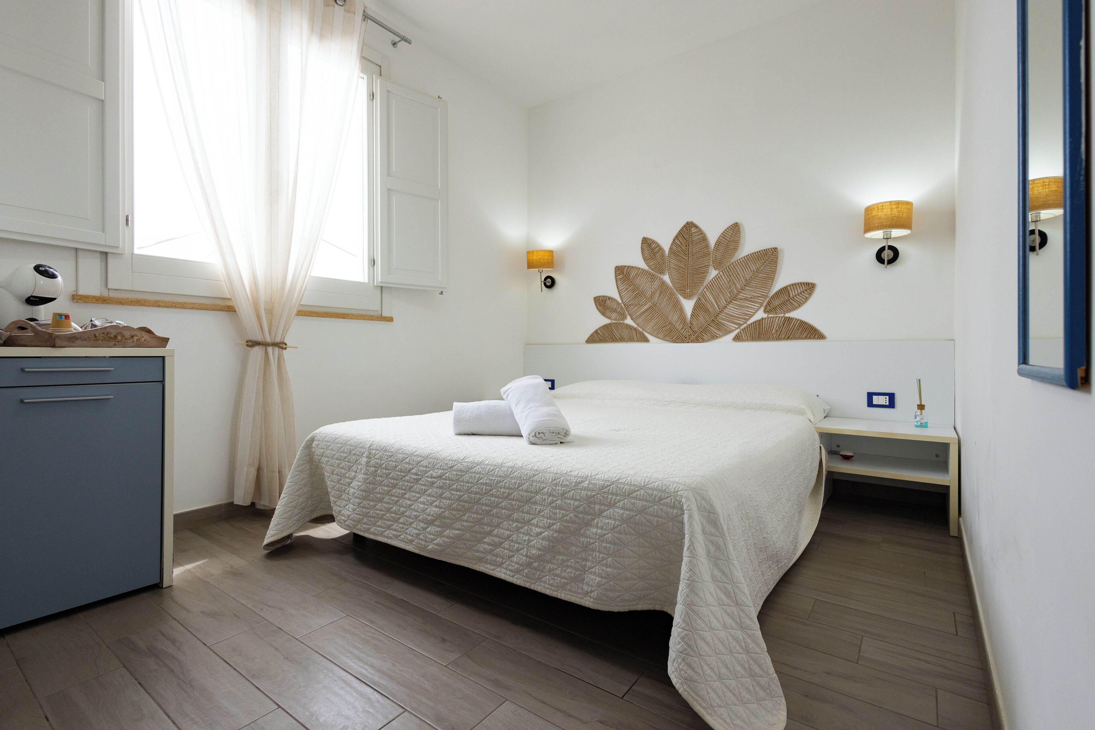 A hotel room with a bed, a desk, a lamp, a mirror, and a window with curtains.