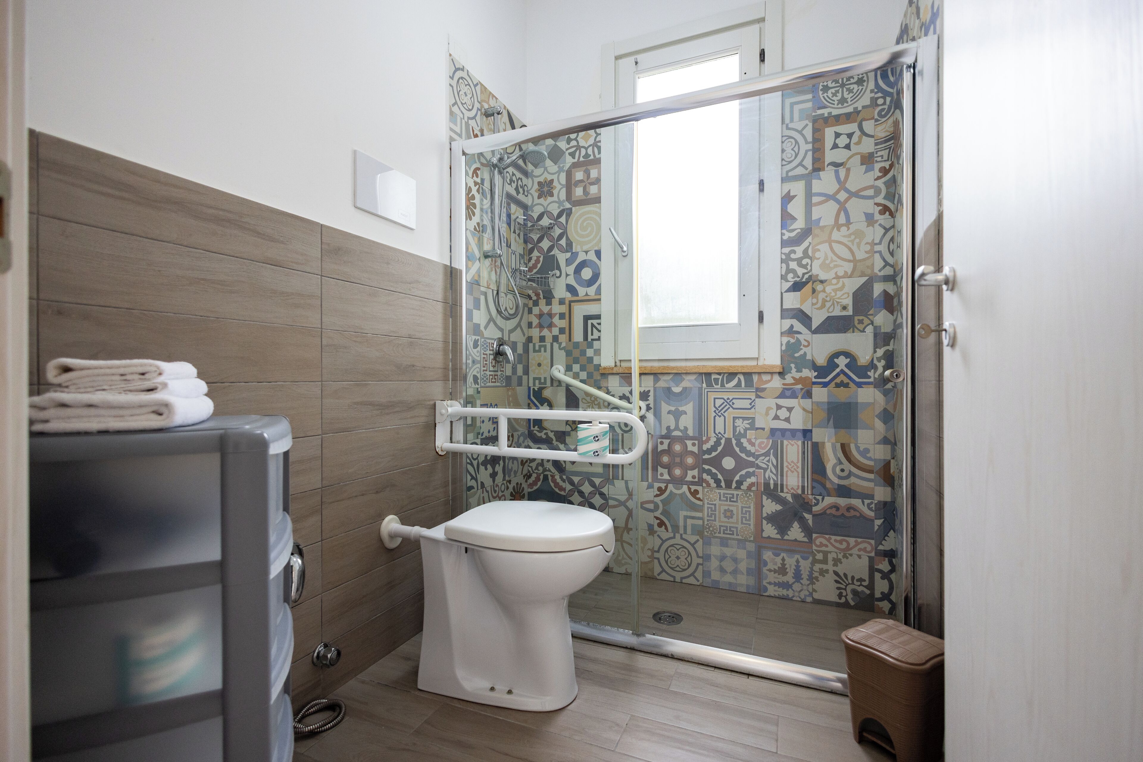 Un baño con inodoro, ducha con puerta de cristal y pared de azulejos estampados.