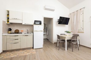 Eine kompakte Küche mit Mikrowelle, Kühlschrank und Herd, ein Essbereich mit Tisch und Stühlen sowie ein an der Wand montierter Fernseher.