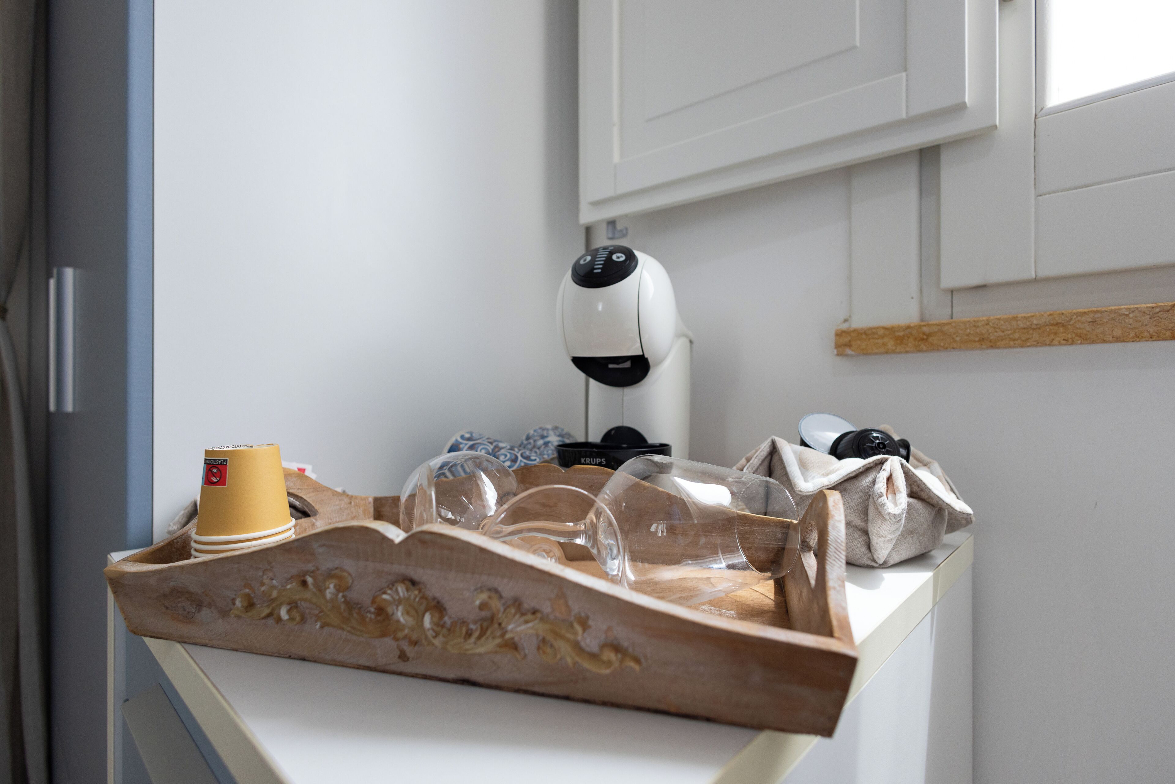 Un taulell de cuina amb una cafetera, un safata amb gots i una tassa.