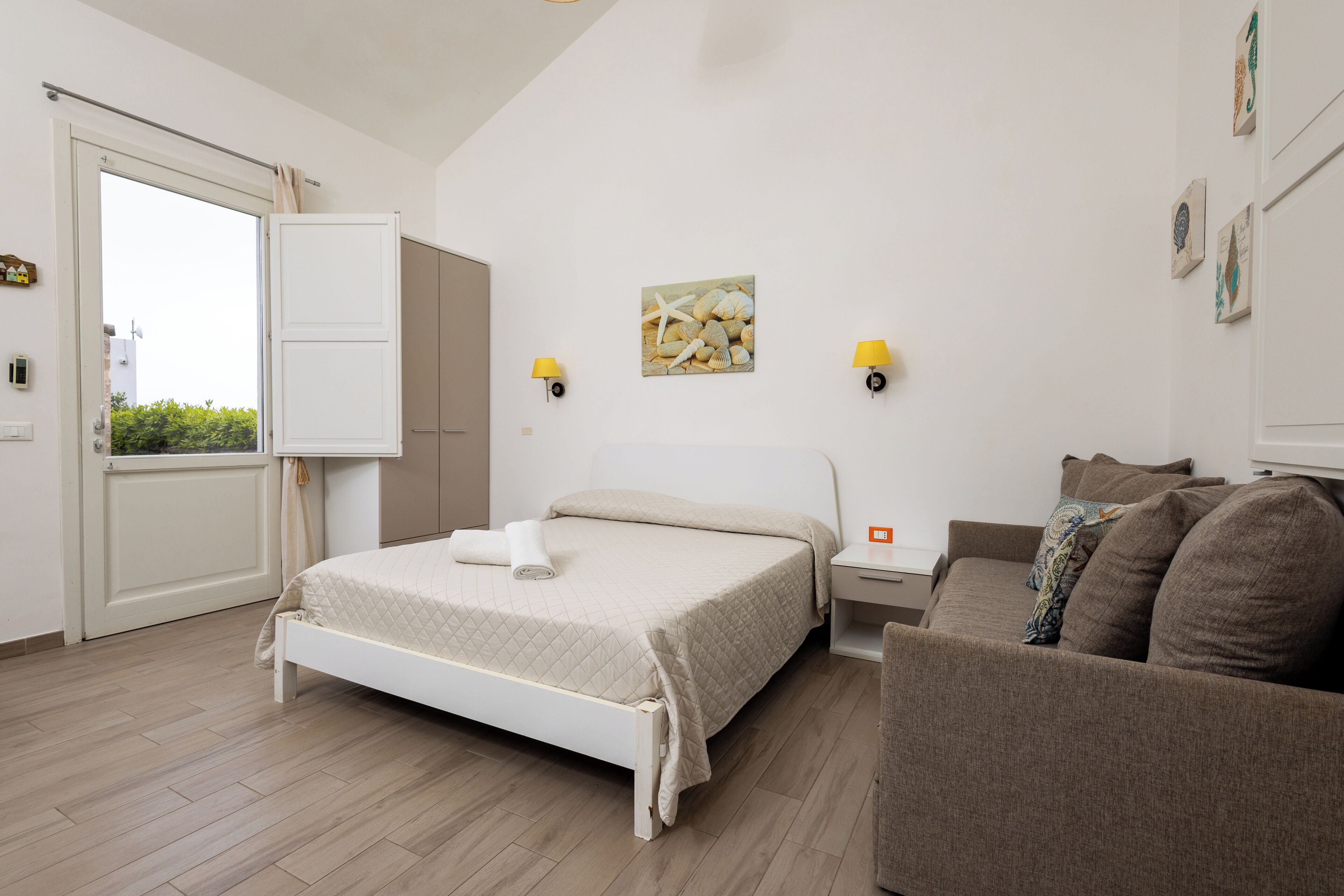 Een slaapkamer met een bed, nachtkastje, bank, raam en wanddecoratie.