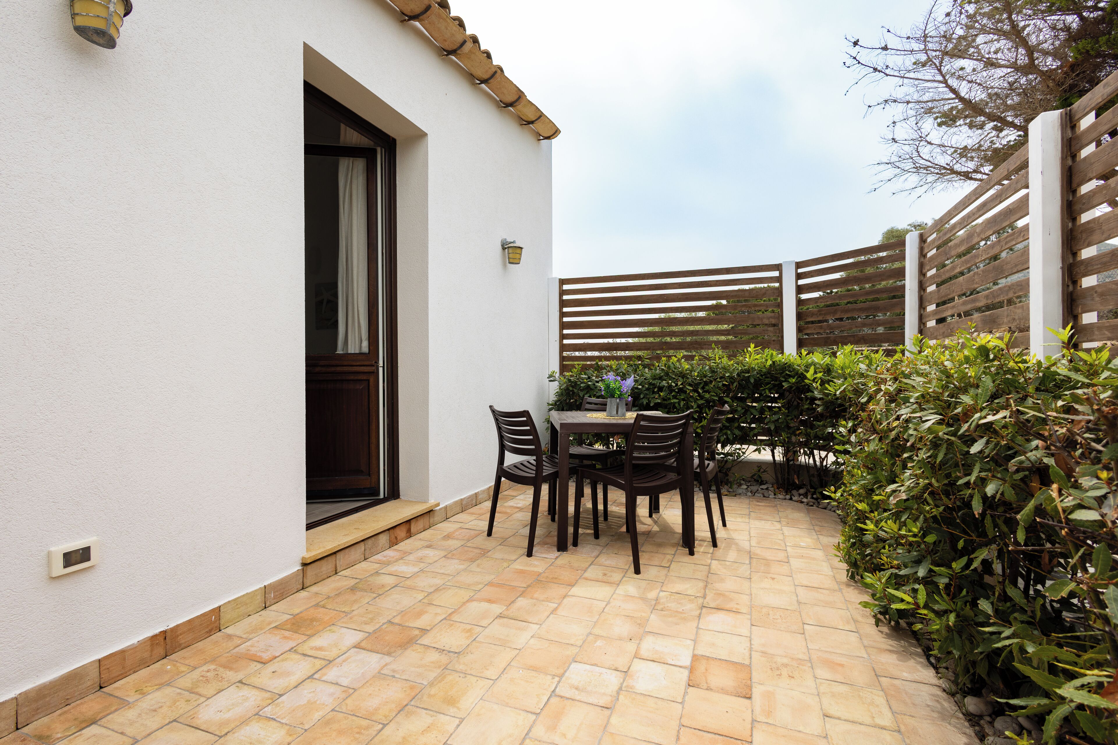 An outdoor patio with a table and chairs, a white building, and a wooden fence.