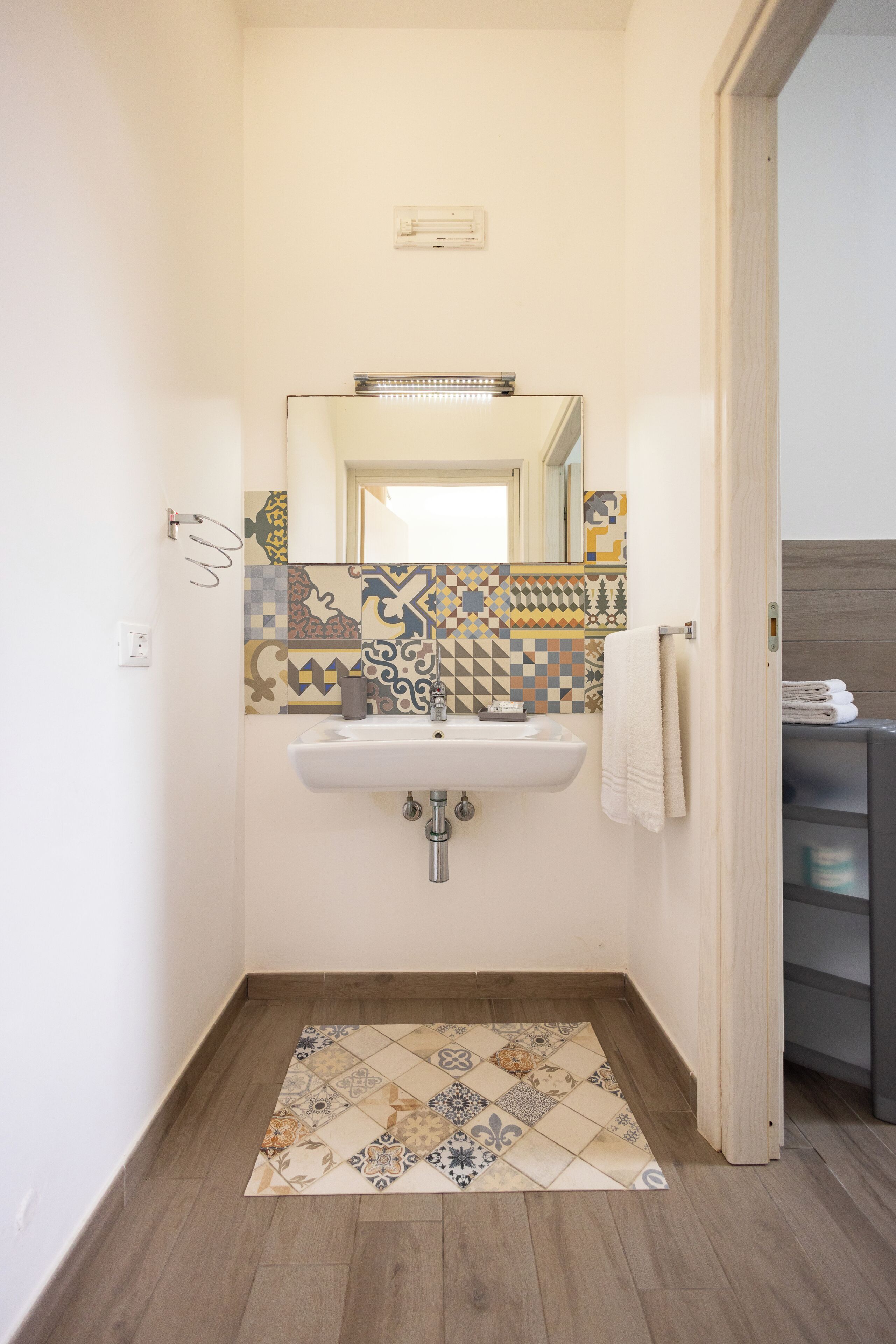 Een badkamer met een wastafel, spiegel, betegelde vloer en houten vloer.