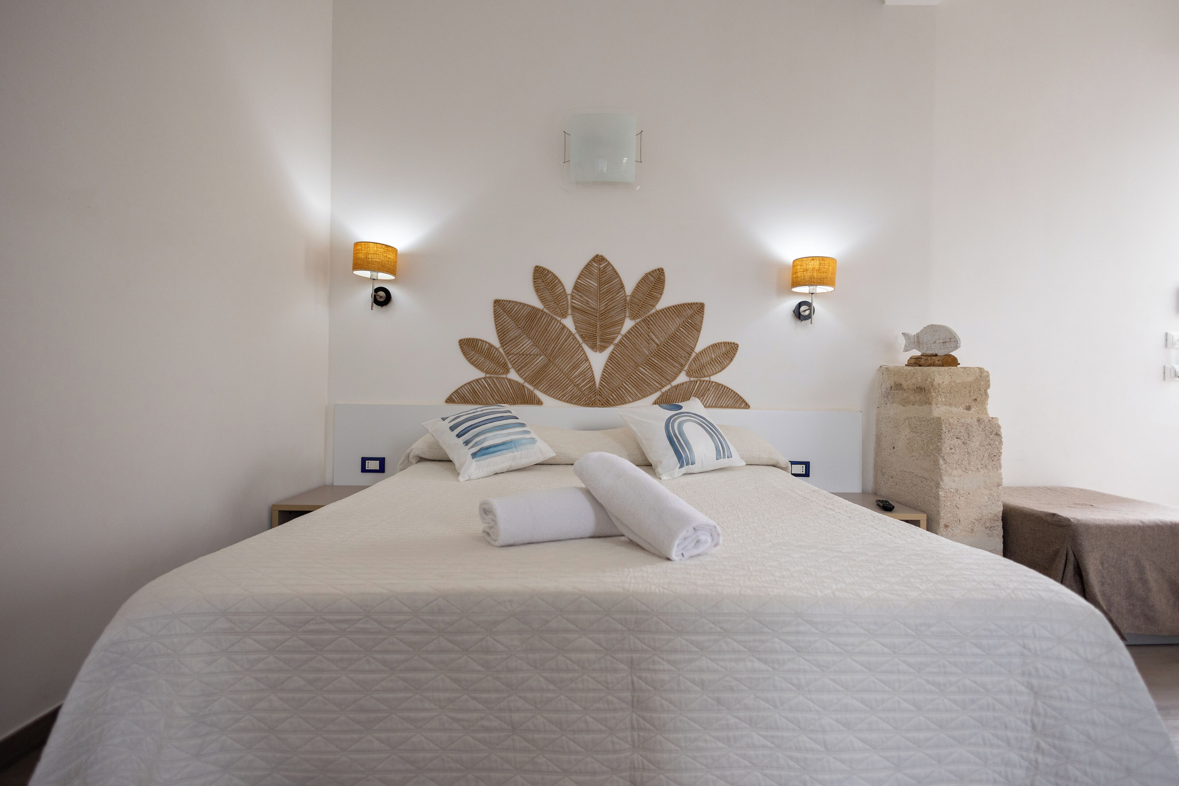 A neatly made bed with a geometric-patterned bedspread, two wall-mounted lamps, and a decorative wall piece.