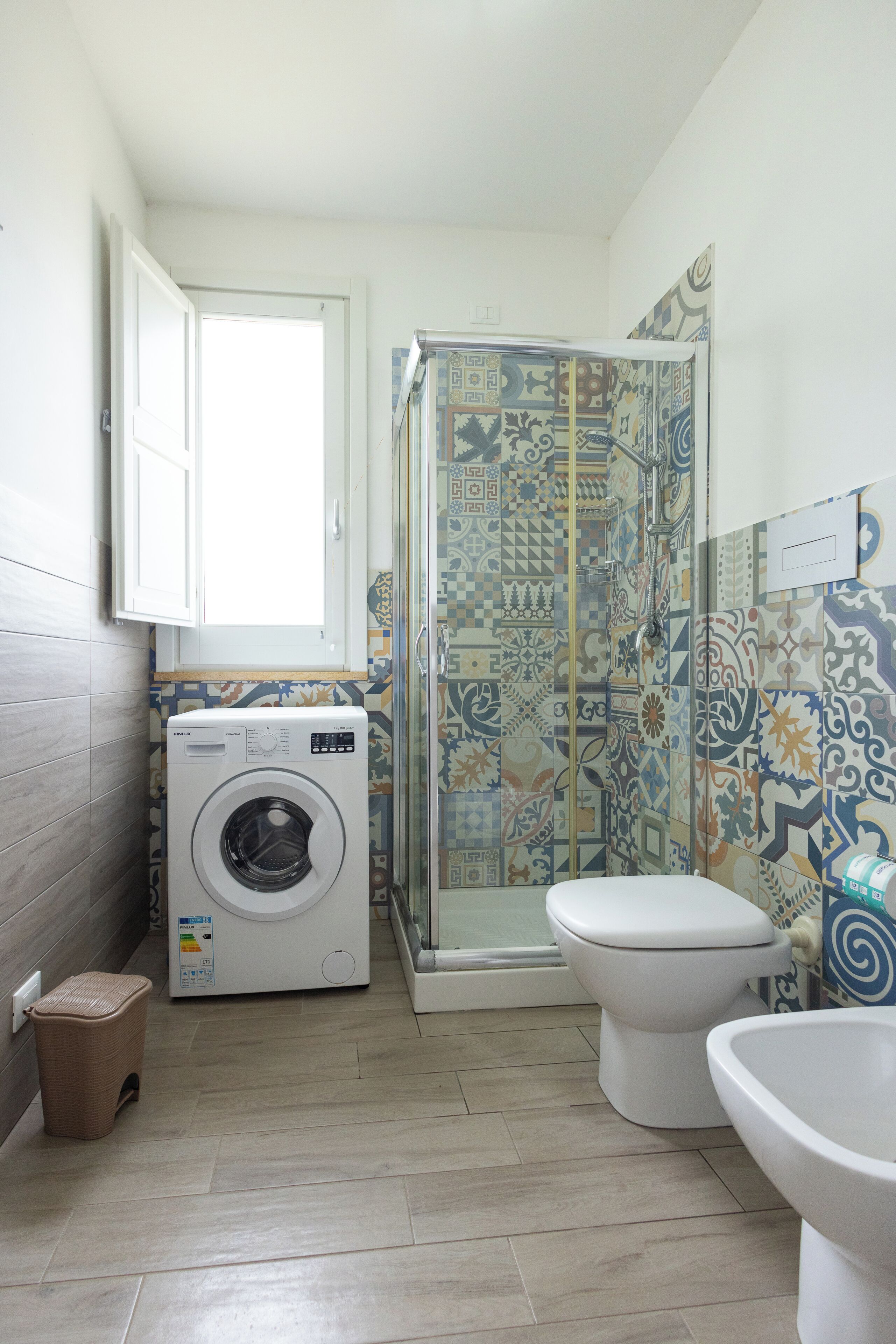 A compact bathroom with a washing machine, toilet, and shower.
