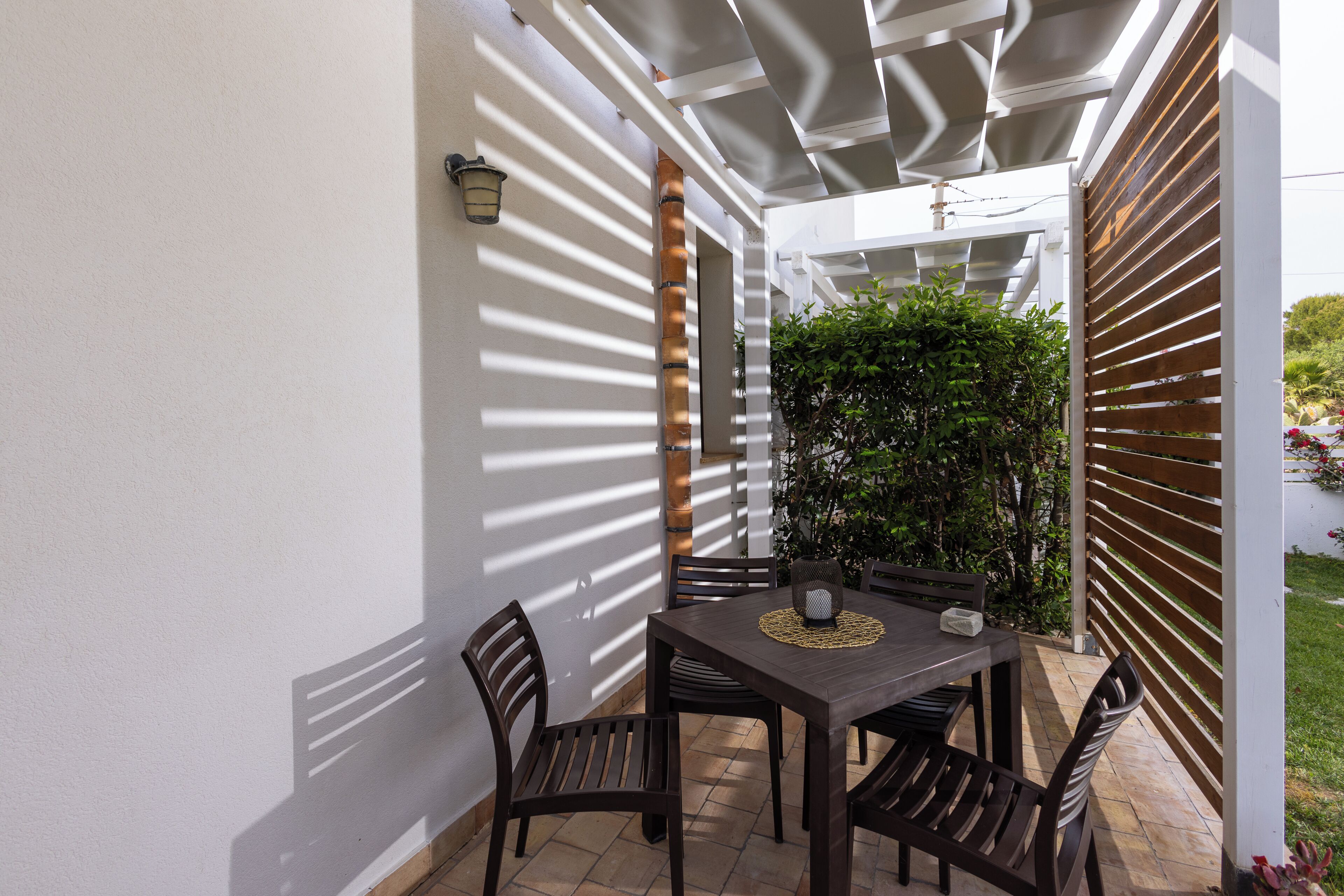 A covered patio with a table and chairs, a wall-mounted lamp, and a wooden fence.