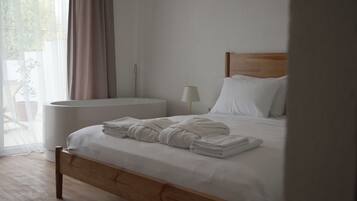 A neatly made bed with folded towels, a bedside table with a lamp, and a view of the outdoors through sheer curtains.
