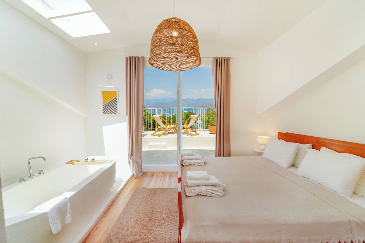 A modern hotel room with a large bed, a bathtub, and a balcony with a view.