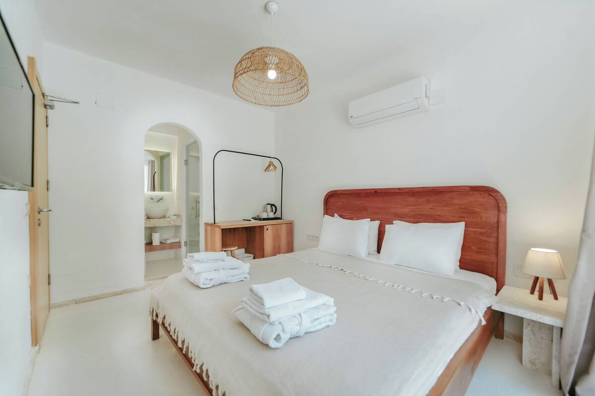 A neatly arranged hotel room with a bed, a desk, a mirror, and a hanging light fixture.