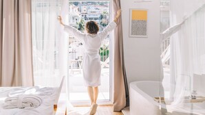 Una habitación con una cama, una ventana con cortinas, una bañera y vistas a edificios.