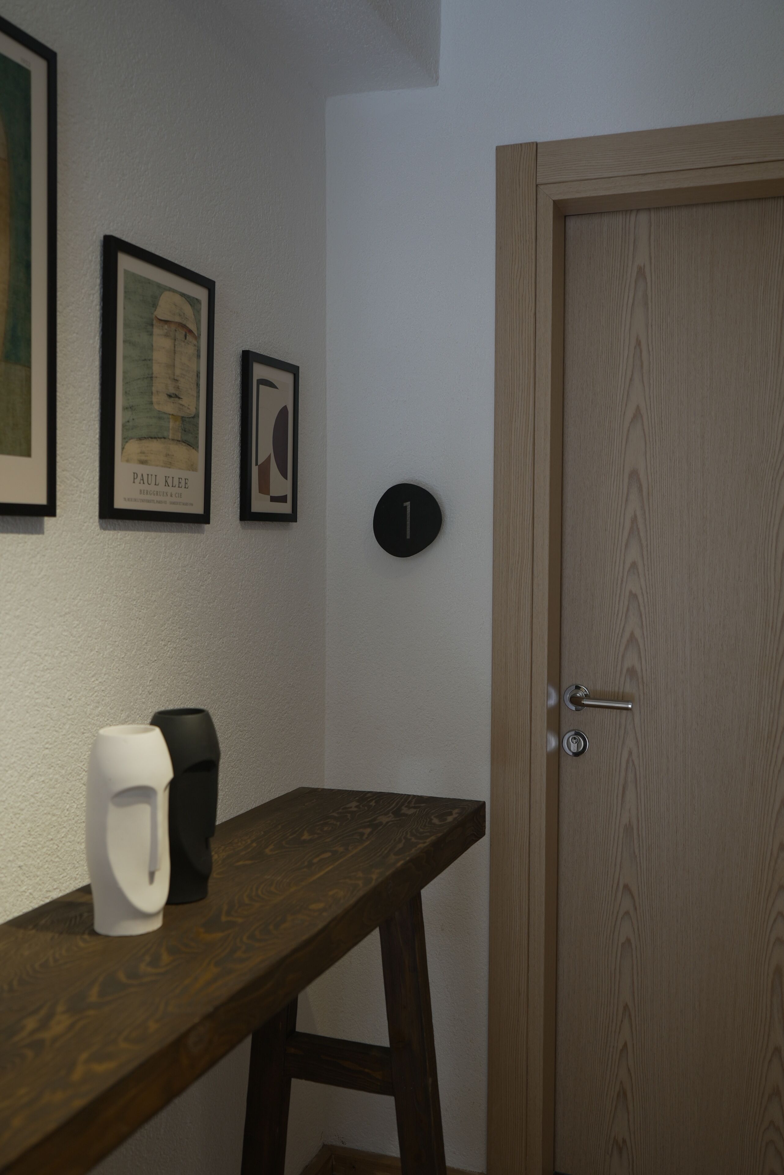 A wooden bench with a white object on it, a door with a number plate, and two framed pictures on the wall.