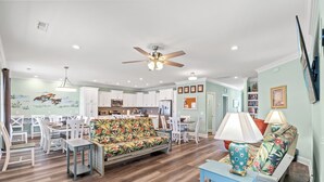 A spacious living area with a sofa, dining table, and chairs, a kitchen in the background, and a ceiling fan. - Just Coasting - Saltwater Pool, 5 Bedrooms, Across Street to Beach (North Myrtle Beach)