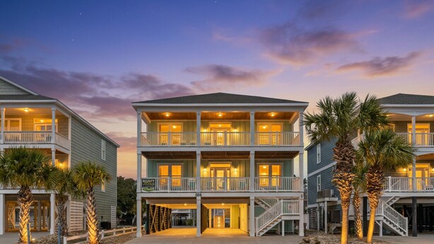 A multi-story hotel with balconies, a covered entrance, and palm trees. - Just Coasting - Saltwater Pool, 5 Bedrooms, Across Street to Beach (North Myrtle Beach)