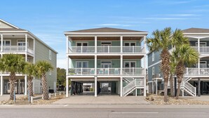 A beachfront multi-story hotel with balconies, palm trees, and a clear sky. - Just Coasting - Saltwater Pool, 5 Bedrooms, Across Street to Beach (North Myrtle Beach)
