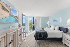 A modern hotel room with a large bed, a desk, a view of the pool, and a cityscape.