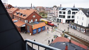 Une gare avec un train rouge, un bâtiment blanc avec une enseigne, et un bâtiment avec un toit rouge, également doté d’une enseigne.