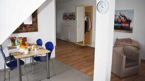 Un coin repas avec une table mise pour le petit-déjeuner, une horloge au mur et un porte-manteau avec des vêtements suspendus.