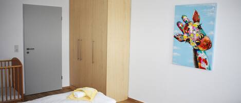 A bedroom with two beds, a wooden wardrobe, and a giraffe painting on the wall.