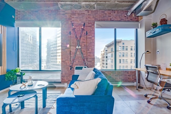 Charming vintage-style living room with a simulated brick accent wall and large windows showcasing stunning 8th-floor city views