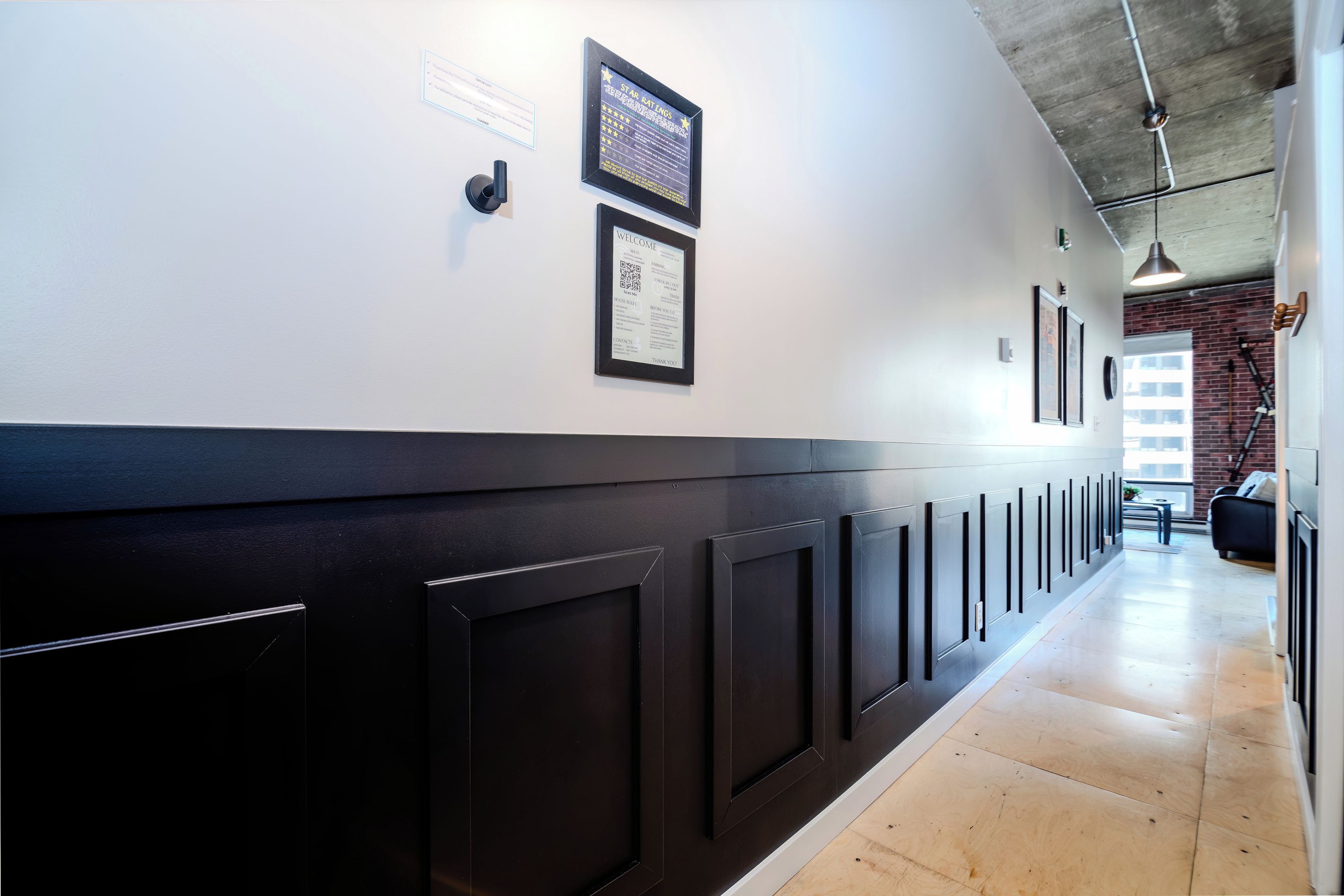 A hallway with black paneling, framed welcome signs, and a brick wall in the background.