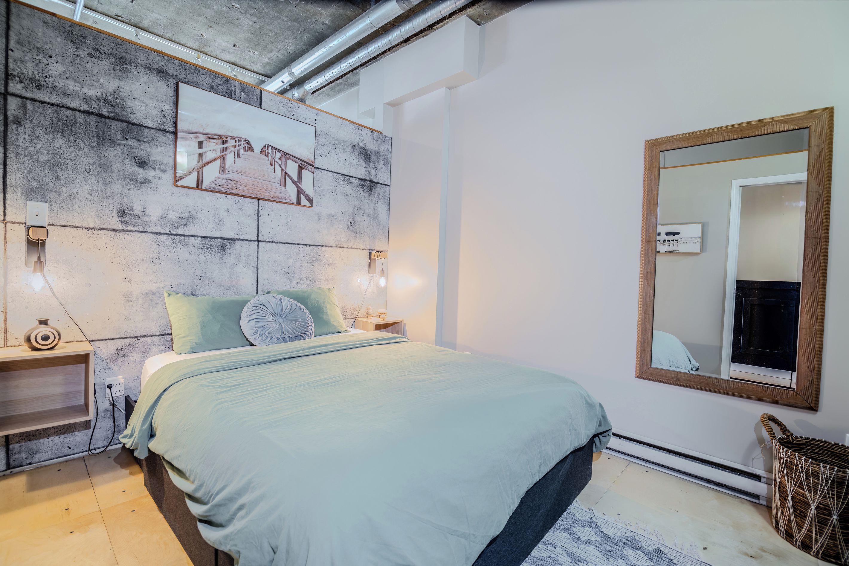 Une chambre à coucher comprenant un lit, une tête de lit décorée, une table de chevet, une commode, un miroir et un radiateur fixé au mur.