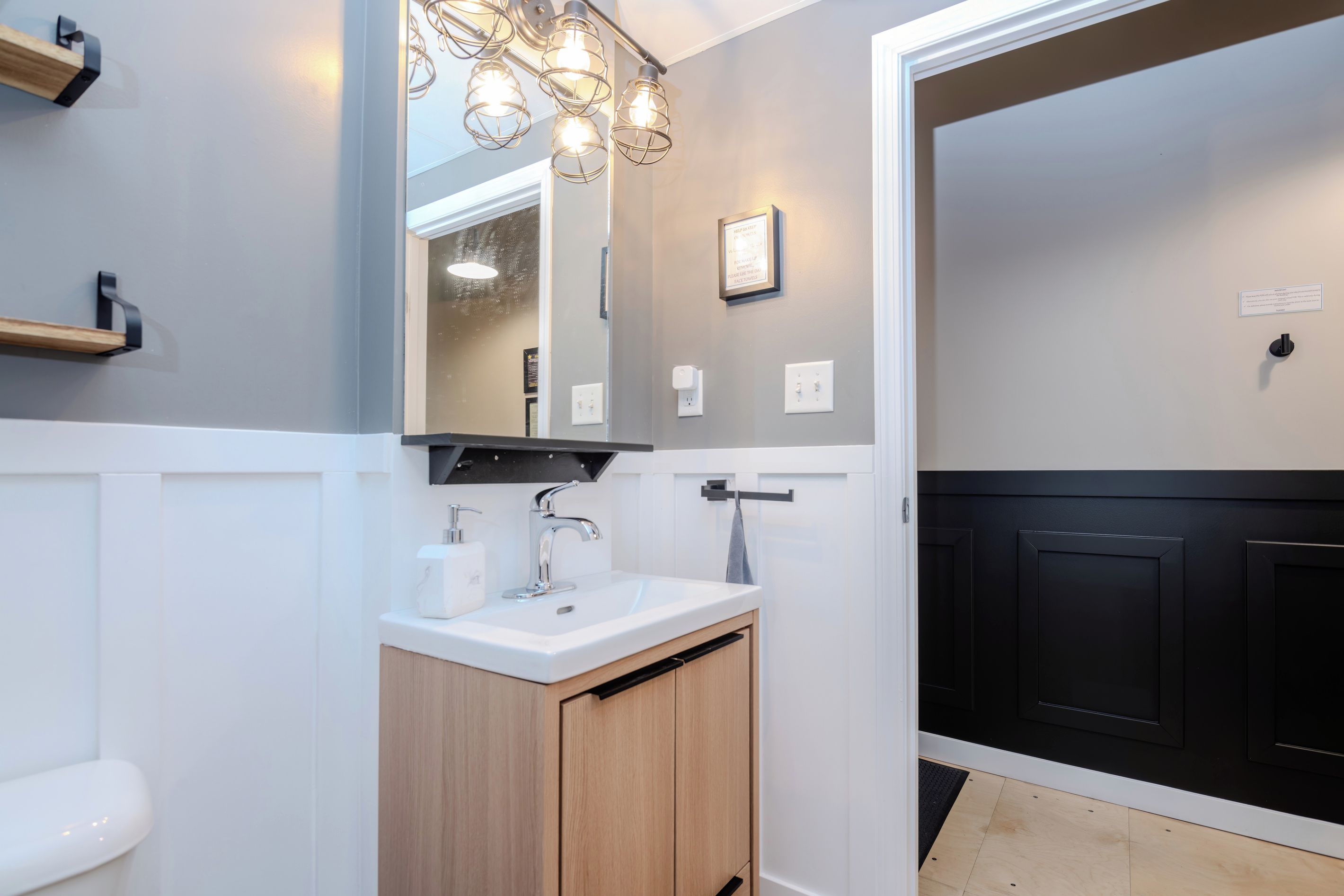 A modern bathroom with a white sink, wooden cabinet, and a black door.