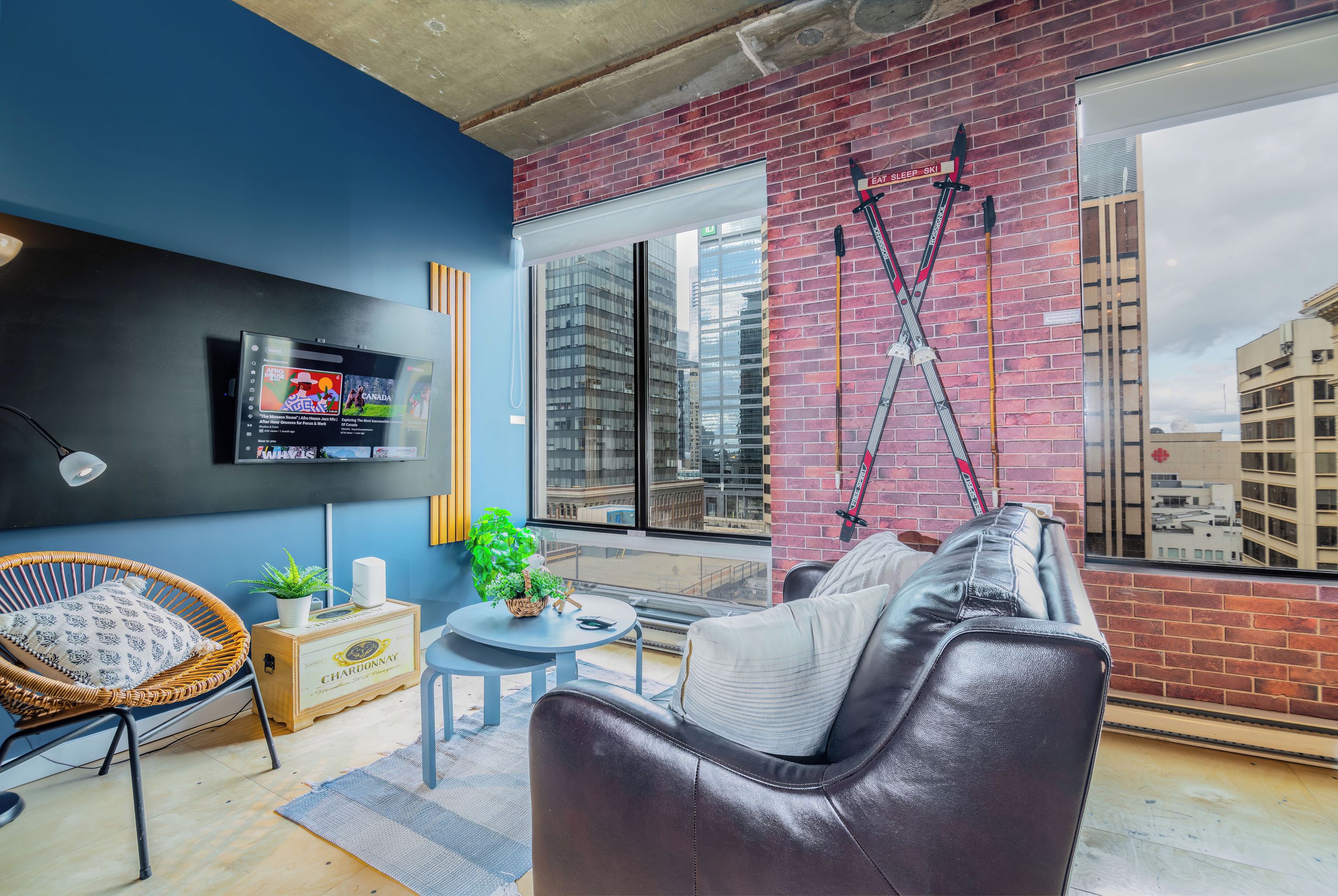 A modern living room with a sofa, a TV, a plant, and a window with a city view.