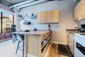 Cocina compacta con una isla de madera, horno empotrado y ventana con vistas a un edificio de ladrillo.