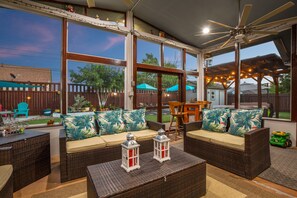 Un patio cubierto con mobiliario de mimbre, ventilador de techo y luces colgantes.