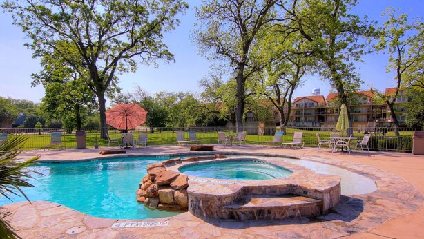 A swimming pool with a hot tub, surrounded by lounge chairs and a large umbrella. - Waterwheel Ww B202 2 Bedroom Condo by RedAwning (New Braunfels)