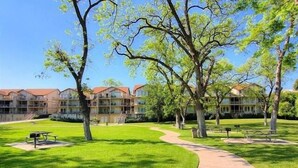 A courtyard with a paved walkway, picnic tables, and a building with multiple balconies. - Waterwheel Ww B202 2 Bedroom Condo by RedAwning (New Braunfels)