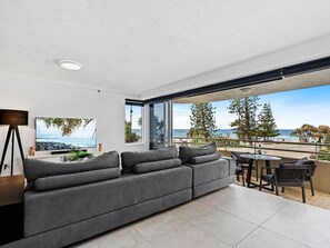 A modern living room with a grey sofa, a coffee table, and a view of the ocean through large windows. - Beachfront Escape Zenith - Ocean Views, Pool, Spa (Surfers Paradise)