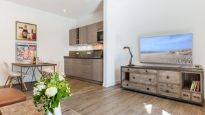 A modern living room with a dining area, a kitchen, and a large flat-screen TV on a wooden console. - Exklusiv. Strandnah. Zentral (Westerland)