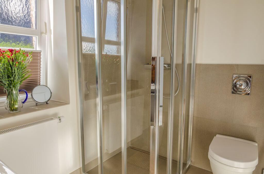 A bathroom with a glass shower enclosure, a toilet, and a window with a view of greenery.