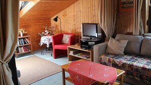 Une pièce chaleureuse avec un plafond en bois, un fauteuil rouge, un canapé, un téléviseur et une bibliothèque.