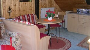 Un intérieur chaleureux, avec des éléments en bois, comprenant un coin repas, un canapé et une cuisine.