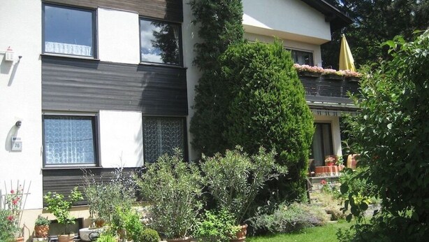 Un bâtiment moderne à deux étages, doté d’un jardin bien entretenu, comprenant des plantes en pot et une pelouse.