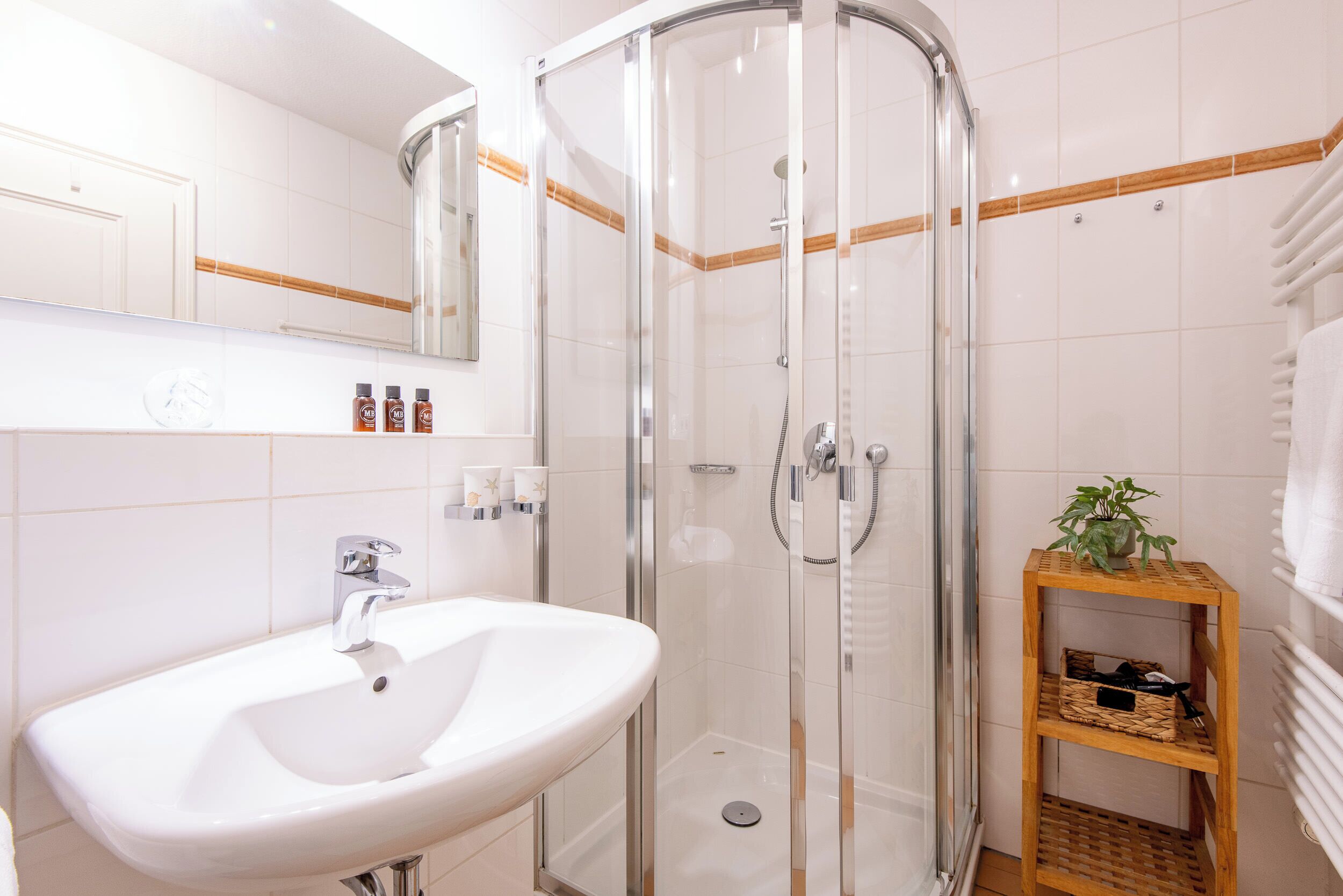 A modern bathroom with a glass-enclosed shower, a white sink, and a wooden shelf with toiletries.