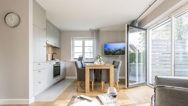 A modern kitchen with a dining area, a TV, and a large window. - Modern. Ruhig. Südterrasse (Westerland)