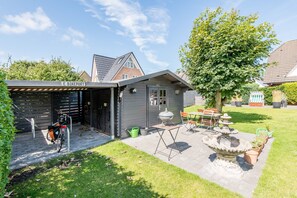 A house with a covered garage labeled "E BIKEPORT," a barbecue grill, a bicycle, and a stone fountain in the yard.