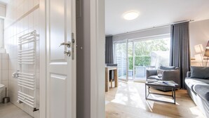 A modern bathroom with a white towel rack and a toilet. The room has a wooden floor and a large window with curtains. - Modern. Ruhig. Südterrasse (Westerland)