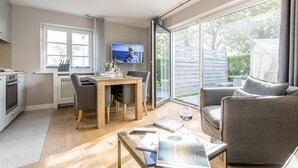 A modern living room with a television, a dining area, and a large window offering a view of the outdoors. - Modern. Ruhig. Südterrasse (Westerland)